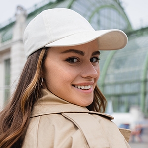 Casquette de baseball blanche avec bord incurvé. Personne portant un manteau beige et une casquette, regardant par-dessus l'épaule à l'extérieur.