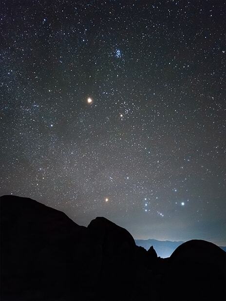 Une photo de paysage nocturne avec la silhouette d'un terrain montagneux au premier plan. Les …